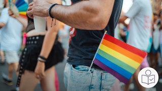 Ein Mann beim Christopher Street Day. Er hat in der Tasche seiner Hose eine kleine Regenbogen·fahne stecken. Rechts das SWR Logo für Leichte Sprache.