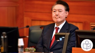 Yoon Suk Yeol sitzt in einem Gerichts·raum. Yoon Suk Yeol war der Präsident von Süd·korea. Rechts das SWR Logo für Leichte Sprache.