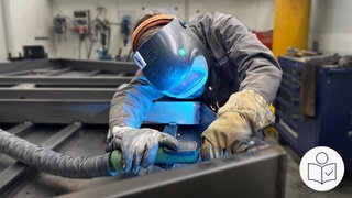 Ein Mann bei der Arbeit. Der Mann hat einen Schutz·helm auf und Hand·schuhe an. Der Mann arbeitet an einem Metall·stück. Viele Hand·werker machen Teile für die Rüstungs·industrie. Rechts das SWR Logo für Leichte Sprache.