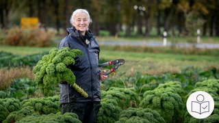 Eine ältere Frau steht auf einem Feld. Auf dem Feld wächst Grün·kohl. Die Frau hat Grühn·kohl in der Hand. Landwirte in Baden-Württemberg wollen weniger Gemüse anbauen. die Landwirte können nicht so viele Mitarbeiter bezahlen. Das liegt am hohen Mindest·lohn. Rechts das SWR Logo für Leichte Sprache.