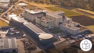 Das neue Kranken·haus in Calw von oben. Es sind mehrere Gebäude und ein Park·haus. Zur Klinik gehört auch eine Notaufnahme und eine Haus für Seelische Gesundheit. Rechts das SWR Logo für Leichte Sprache.