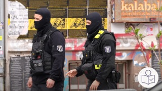 Zwei Polizisten laufen an einem Haus vorbei. Die Polizisten haben ihre Gesichter bedeckt. Rechts das SWR Logo für Leichte Sprache.