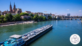 Ein Schiff fährt auf dem Rhein durch die Stadt Basel. Das Grund·wasser in diesem und anderen Gebieten am Rhein hat Schad·stoffe. Rechts das SWR Logo für Leichte Sprache.