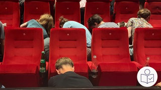 Menschen knien vor roten Kino·sessel. Die Menschen bauen die Kino·sessel ab. Denn das Kino Schauburg in Karlsruhe hat ihnen die Kino·sessel geschenkt. Rechts das SWR Logo für Leichte Sprache.