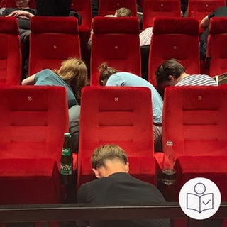 Menschen knien vor roten Kino·sessel. Die Menschen bauen die Kino·sessel ab. Denn das Kino Schauburg in Karlsruhe hat ihnen die Kino·sessel geschenkt. Rechts das SWR Logo für Leichte Sprache.