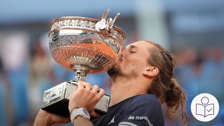 Der Tennis·spieler Alexander Zverev küsst einen Pokal. Den Pokal hat er für seinen Sieg bekommen. Alexander Zverev hat den Wettbewerb French Open gewonnen. Rechts das SWR Logo für Leichte Sprache. 