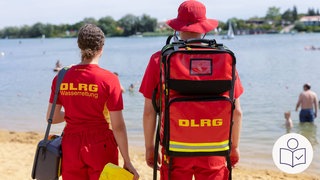 Zwei Helfer von der Deutschen Lebens·rettungs·gesellschaft DLRG an einem Bade·see. Sie haben rote Kleindung an. Einer trägt einen Rettungs·rucksack. Rechts das SWR Logo für Leichte Sprache.