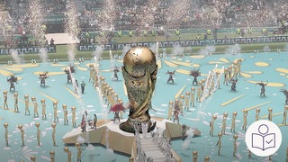 Ein großer WM-Pokal in einem Stadion. Daneben tanzen Menschen. Rechts das SWR Logo für Leichte Sprache.