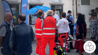 Menschen stehen in Bad Kreuznach vor einem Info-Stand. Der Info-Stand ist von der AfD. Es gab einen Angriff auf den Info-Stand. Rechts das SWR Logo für Leichte Sprache.