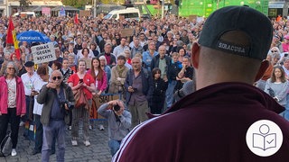 Menschen machen eine Demo. Sie demonstrieren gegen Rechts·extremismus. Im Vordergrund sieht man einen Mann. Der Mann redet zu den Menschen. Rechts das SWR Logo für Leichte Sprache. 