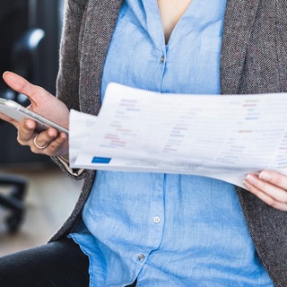 Frau im Büro hält Unterlagen und ein Smartphone in der Hand