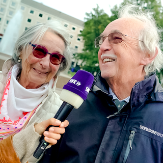 Tici interviewt die Eheleute Helen und Klaus-Peter zum Thema Liebe. Helen und Klaus-Peter lachen in die Kamera. 
