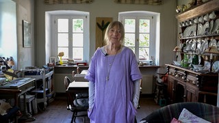 Eine Frau mit blonden Haaren und lila Kleid lächelt in die Kamera.