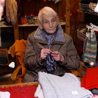 Ältere Dame sitzt in einem Weihnachtsmarkt Häuschen und verkauft Stricksachen.