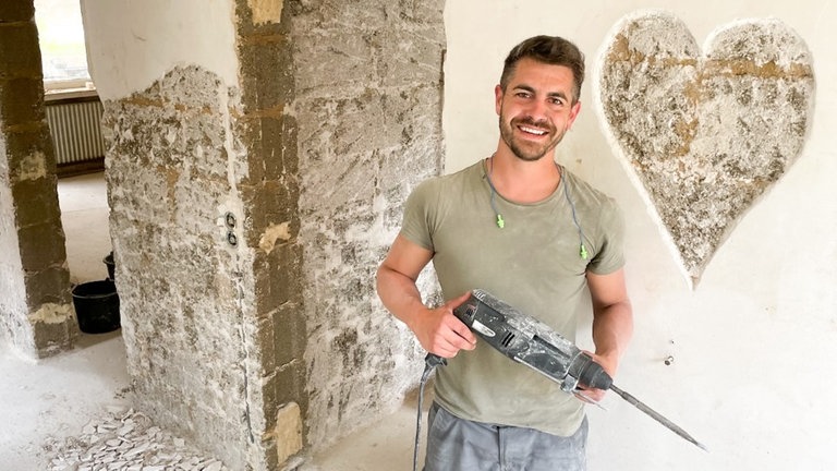 Ein junger Mann steht in Arbeitskleidung in einem von der Flut geschädigten Haus. Er hat ein Herz in die Wand gehämmert. 