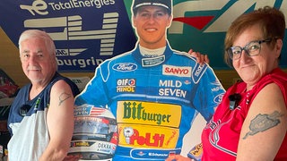 Ein Mann und eine Frau stehen neben einem Pappaufsteller von Michael Schuhmacher, haben ihr T-Shirt hochgezogen und zeigen am Oberarm ein Tattoo des Nürburgrings.