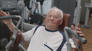Werner geht mit 97 Jahren zweimal die Woche ins Fitnessstudio. Er trainiert an einem Sportgerät und schaut dabei in die Kamera.