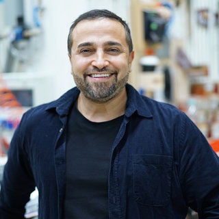 Ehemann Murat Özcan von Sallys Welt steht in einer Werkstatt und schaut lächelnd in die Kamera.