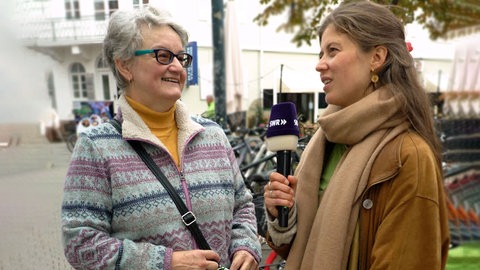  Rentnerin spricht mit Reporterin Tici von SWR Heimat in der Karlsruher Innenstadt.