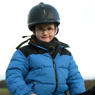 Junge mit Brille in blauer Jacke mit Reiterhelm