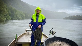 Mann in Regenjacke auf einem Boot vor Bergen.