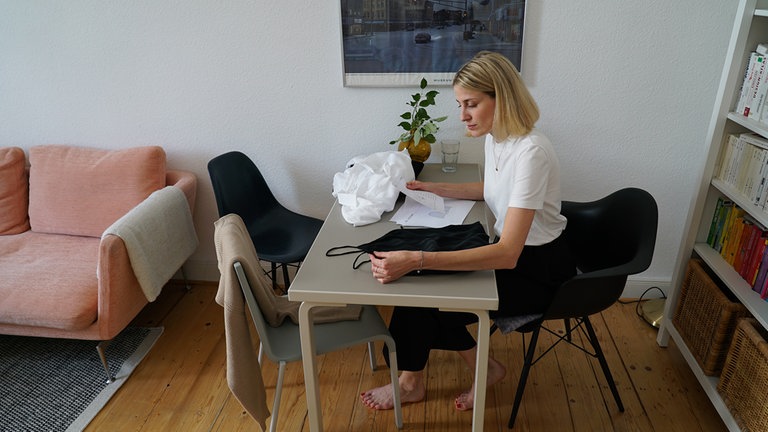 Hannah sitzt an einem Tisch und hält ihre entworfenen Kleidungsstücke in der Hand. 