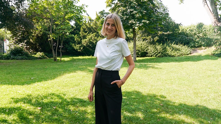 Hannah, Gründerin eines nachhaltigen Modelabels, steht auf einer grünen Wiese. 