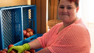 Eine Frau steht vor einigen Kisten, die mit Äpfeln gefüllt sind.