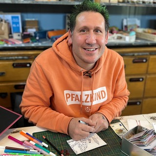 Mann mit grünen Haaren und orangenem Pullover.