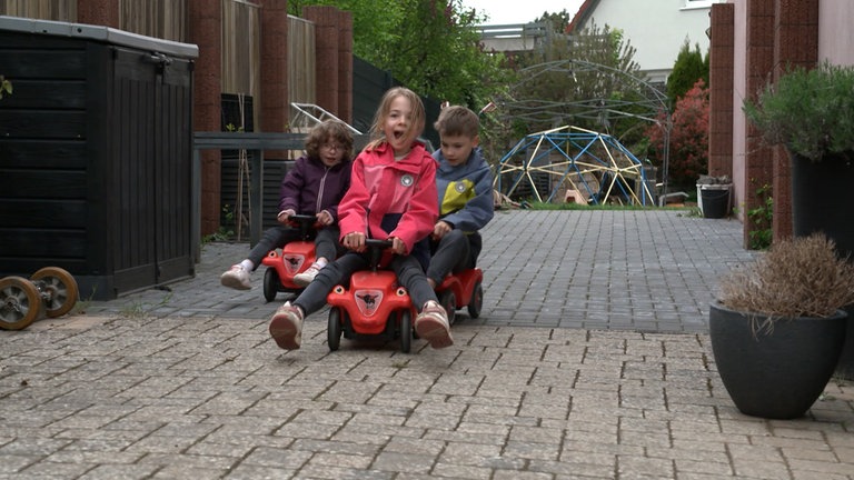 Drei Kinder fahren mit Bobbycars durch den Hof.