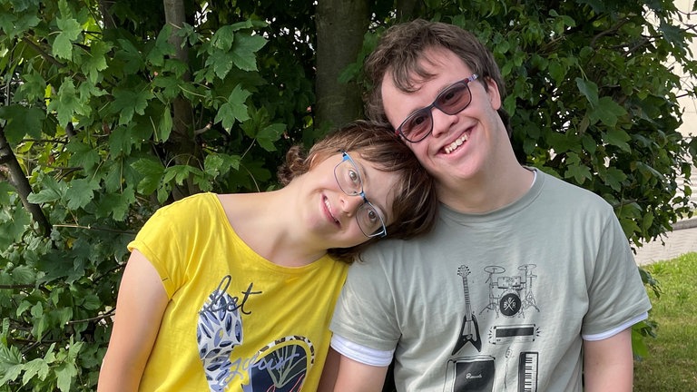 Zwei junge Menschen stehen im Freien Arm in Arm nebeneinander