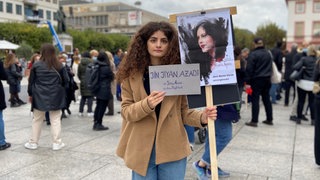 Eine junge Frau hält in Mainz bei einer Demo für Freiheit im Iran zwei Schilder in den Händen.