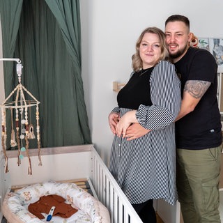 Junges Ehepaar steht in Kinderzimmer und umarmt sich.