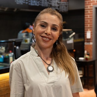 Frau mit blonden Haaren steht vor einer Theke und lächelt in die Kamera.