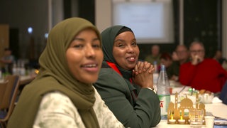 Junge Frau mit Hijab sitzt an einem langen Tisch.