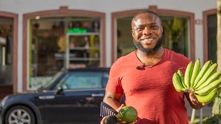 Junger Mann mit Bananen, Avocados und einem Kamm vor seinem Laden