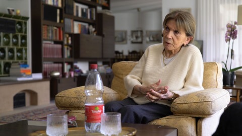 Ruth ist 95 Jahre alt und Zeitzeugin des Zweiten Weltkriegs. SWR Heimat hat sie zu Hause besucht und sie erzählt von ihren Erlebnissen während dem Krieg. Sie sitzt auf dem Sofa in ihrem Wohnzimmer.