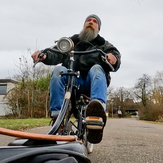 Michael fährt auf einem seiner selbstgebauten Fahrräder, durch einen Park.