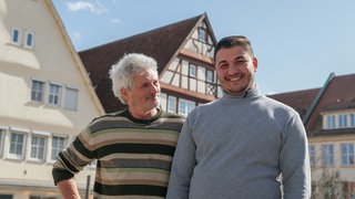Ralf und Muath stehen nebeneinander auf dem Nürtinger Schillerplatz und schauen in die Kamera. Über die letzten drei Jahre sind die beiden sehr gute Freunde geworden.