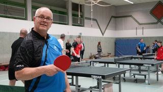 Älterer Herr mit Tischtennisschläger vor Platte