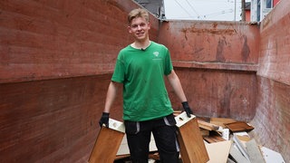 Junger blonder Mann in grünem T-Shirt mit Arbeitshandschuhen.