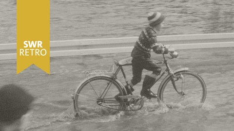 SWR Retro: Junge fährt auf dem Fahrrad durch Hochwasser