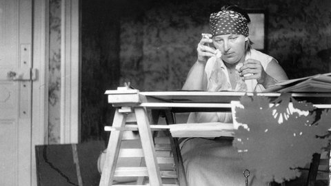 Lotte Reiniger an ihrem Schreibtisch mit zwei Scherenschnittfiguren. 