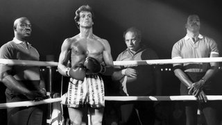 Rocky Balboa steht im Ring vor einem Kampft. Hinter ihm sind seine Trainer zu sehen.