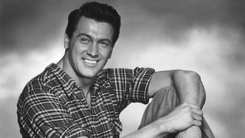 Rock Hudson sitzend, mit angewinkeltem Bein, Promo-Aufnahme Mitte der 1950er-Jahre