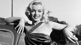 Marilyn Monroe lehnt sich lächelnd an ein Sportauto.