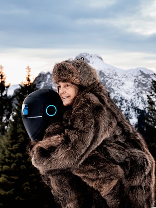 Eine alte Frau im Pelzmantel wird von einem Roboter durch eine schneeverschneite alpine Landschaft getragen (Ausschnitt aus dem Film "Frau Winkler verlässt das Haus") 