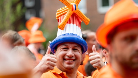 Ein Fan der niederländischen Nationalmannschaft in Orange gekleidet mit einer Kopfbedeckung in Mühlenform. Warum ist Orange eine Art Nationalfarbe der Niederlande? Die einfache Antwort findet man im Namen des Königshauses, denn die niederländischen Könige stammen aus dem Adelshaus Oranien-Nassau.