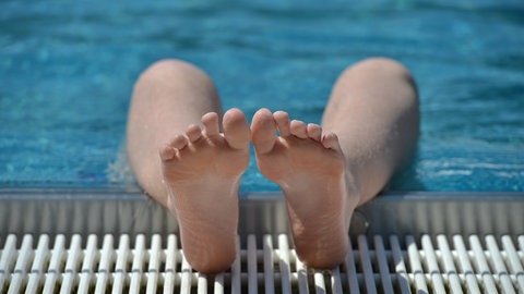 Füße und Unterschenkel am Beckenrand von jemandem, der im Schwimmbecken abgetaucht ist