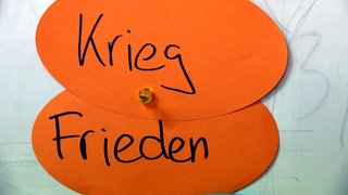 An einer Wand eines Gymnasiums hängen Zettel mit der Aufschrift "Kieg" und "Frieden"